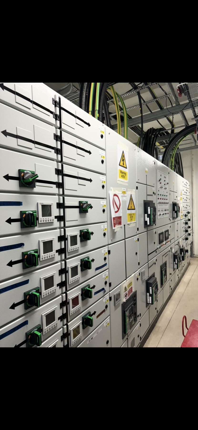 A row of electrical switchgear panels with overhead cables